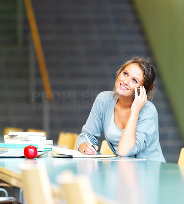 Young charming girl using cellphone while making notes