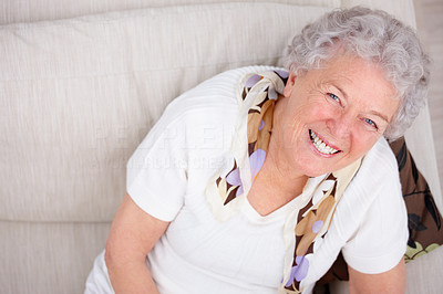 Top view of an old woman smiling and sitting on a sofa