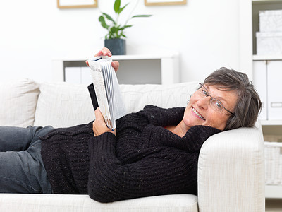 Happy mature woman lying on a sofa reading a book