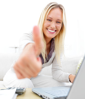 Portrait of a young woman sitting on sofa with a laptop and showing thumbs up sign