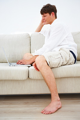 Young guy sitting on sofa and using laptop at home