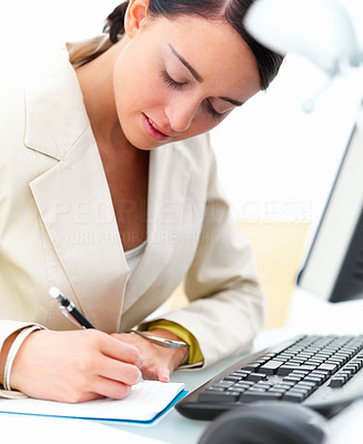 Closeup of a pretty young business woman at desk writing on a book