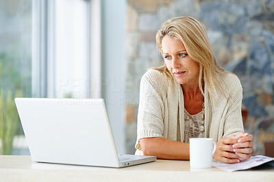 Middle aged woman with coffee cup looking at laptop screen