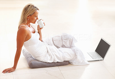 Mature woman drinking tea and using laptop on floor