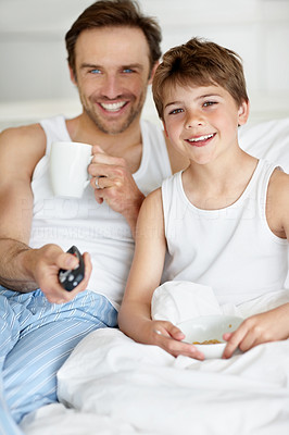 Father and son having breakfast on bed and watching television