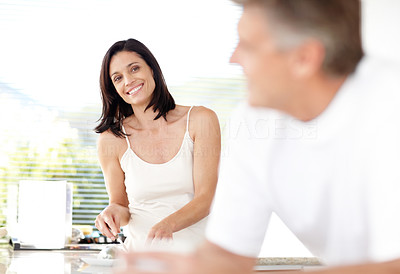 Smiling mature lady working in kitchen with her husband in front