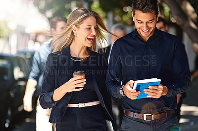 Buy stock photo Shot of two professional coworkers using a digital tablet together while walking outside