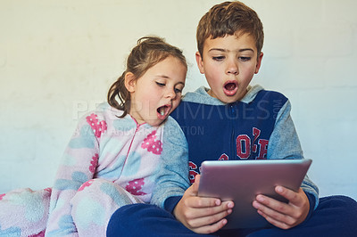 Buy stock photo Cropped shot of two young siblings looking surprised while using a digital tablet at home