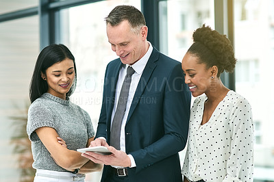 Buy stock photo Cropped shot of three businesspeople looking over a tablet in the office
