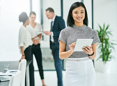 Buy stock photo Cropped portrait of a young businesswoman looking at a tablet in the office with her colleagues in the background