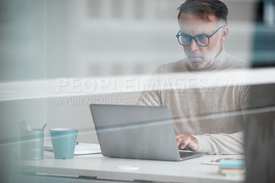 Buy stock photo Cropped shot of a handsome mature businessman using a laptop while sitting at his desk in the office