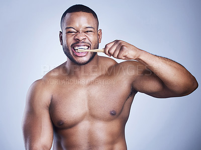 Buy stock photo Studio shot of a handsome young man brushing his teeth against a blue background