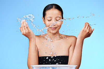 Buy stock photo Shot of a beautiful young woman splashing water on her face against a blue background