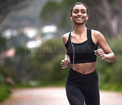Buy stock photo Shot of a sporty young woman wearing earphones while running outdoors