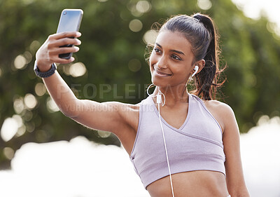 Buy stock photo Shot of a sporty young woman wearing earphones and taking selfies while exercising outdoors