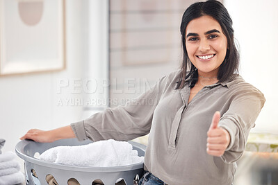 Buy stock photo Shot of a young woman showing a thumbs up while doing laundry at home
