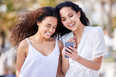 Buy stock photo Shot of two young women using a smartphone during a fun day outdoors