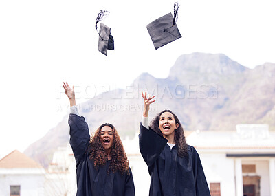 Buy stock photo Shot of two young women throwing their caps in the air on graduation day