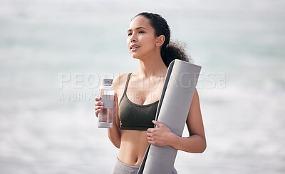 Buy stock photo Shot of a fit young woman holding her yoga mat and water bottle while at the beach