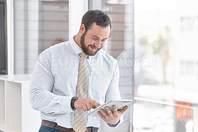Buy stock photo Shot of a young businessman using a digital tablet while standing at a window in an office