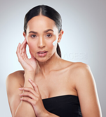 Buy stock photo Studio portrait of a beautiful young woman applying moisturiser to her face against a grey background