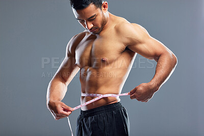 Buy stock photo Studio shot of a muscular young man measuring his waist against a grey background