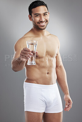 Buy stock photo Studio portrait of a muscular young man posing with a glass of water against a grey background