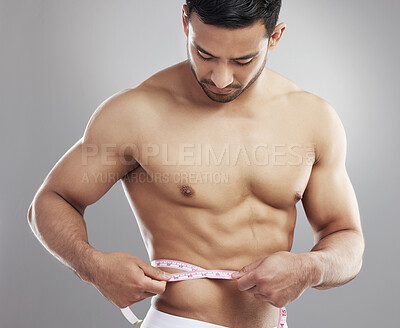 Buy stock photo Studio shot of a man measuring his waist using a measuring tape against a grey background