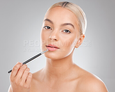 Buy stock photo Shot of a beautiful young woman applying lipgloss to her lips against a grey background