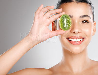 Buy stock photo Studio shot of an attractive young woman holding kiwi fruit to her face against a grey background