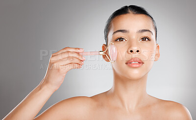 Buy stock photo Studio shot of an attractive young woman using a jade roller on her face against a grey background