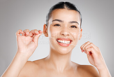 Buy stock photo Studio shot of an attractive young woman flossing her teeth against a grey background