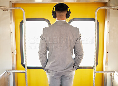 Buy stock photo Rearview shot of a young businessman wearing headphones while standing at the doorway of a train during his commute