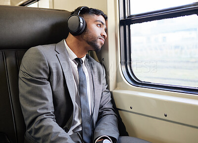 Buy stock photo Shot of a young businessman wearing headphones while staring out the window on a train during his commute