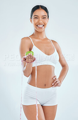 Buy stock photo Shot of an attractive young woman standing alone in the studio while holding an apple and measuring tape
