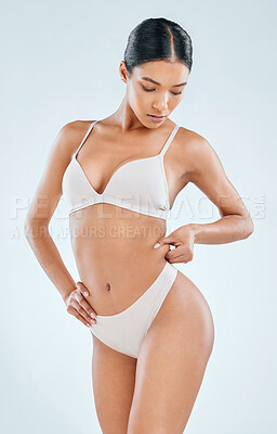 Buy stock photo Shot of an attractive young woman standing alone in the studio and pulling at fat around her waist