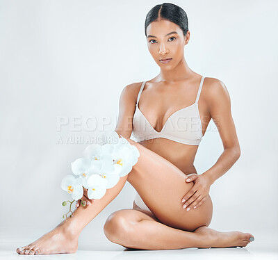 Buy stock photo Full length shot of an attractive young woman sitting alone in the studio and posing while holding orchids