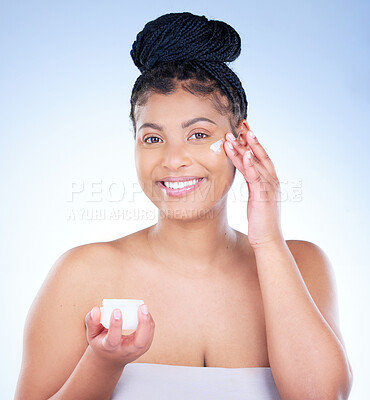 Buy stock photo Studio portrait of an attractive young woman applying moisturiser to her face against a blue background