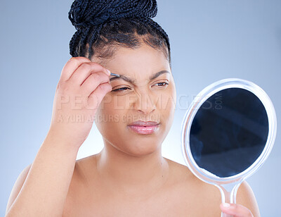 Buy stock photo Studio shot of an attractive young woman tweezing her eyebrows against a blue background