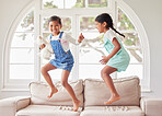 Two girls jumping on the sofa together. Two sisters having fun and looking happy while dancing and playing together at home