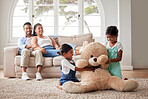 Young couple relaxing on a sofa while their two girls play on the living room floor with their soft teddy at home