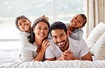 Young happy smiling couple looking cheerful and relaxed while sharing the bed with their daughters. Two girls being playful while in bed with their parents