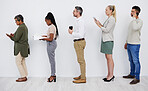 Full length profile of diverse group of businesspeople standing in line together to wait while using technology and paperwork. Team of professionals queueing in row for an interview for a job vacancy 