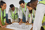 Group of five designers smiling while looking at a blueprint talking together and standing around a table in an office at work. Mature male boss showing his team of workers plans on paper