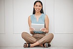 Cheerful young businesswoman using her wireless tablet device, sitting on the floor of her office. Portrait of smiling hispanic business professional using a device to shop online while at work