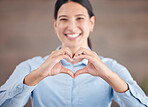 Smiling mixed race businesswoman standing alone and using hand gestures to make a heart shape. Confident and ambitious professional showing heart symbol and sign. Spreading positivity, love and luck