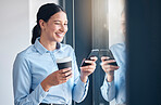 Happy young mixed race businesswoman using social media on a phone while drinking a cup of coffee on a break and standing at a window in an office at work. One cheerful hispanic female texting at work
