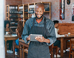 Young african american businessman wearing a apron working in a retail store using a digital tablet device. Portrait of a smiling small business owner, entrepreneur buying stock online using wireless technology in a cafe