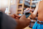 Closeup of unknown mixed race customer using a wireless credit card machine to pay for her coffee. African american barista assisting a woman in a cafe. Contactless paying system during covid pandemic
