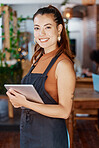 Young hispanic business owner using a wireless tablet in her retail store. Portrait of smiling entrepreneur standing in her restaurant using an online digital device. Young new business owner 